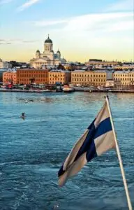Helsinki waterfront with Helsinki Cathedral, historic buildings, and a Finnish flag overlooking the sea.