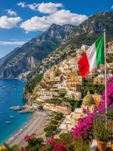 Italian flag overlooking Positano, a colorful coastal town on Italy’s Amalfi Coast, with mountains, beach, turquoise sea, and hillside buildings.